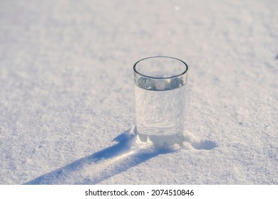 Glass with water on a white snow in winter, close up