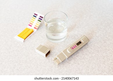 Glass Of Water, Quality Tester And Universal Litmus Ph Tester With Color Scale. Measuring The Characteristics Of Drinking Water. Tap Water Quality Analyzer . Checking The Purity Of Water At Home.