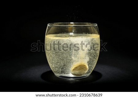 Glass of water with soluble tablet on black background