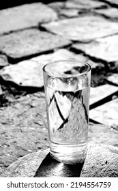 A Glass Of Water Stands On A Gray Broken Paving Slab.