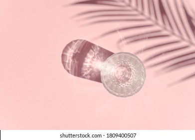 A Glass With Water In Sun Rays Seen Top View. Palm Leaf Shadow.