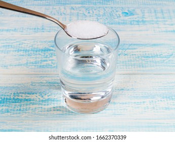 Glass Of Water With Tea Spoon Full Of Salt Above. Salinity Concept.