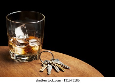 A glass of whiskey and car keys on a table with a black background.