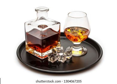 A glass of whiskey with ice or brandy and a square carafe on a black dish isolated against a white background. Whiskey with ice in the glass on a white background.