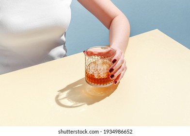 Glass With Whiskey And Ice Cube In Woman Hand On Table On Blue Background. Modern Isometric Style. Creative Concept