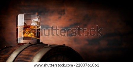 Glass of whiskey with ice cubes on the old barrel. With copy space on wooden background