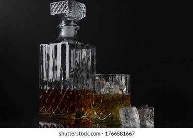 Glass Of The Whiskey With Ice Cubes And A Square Decanter On A Black  Background.