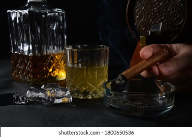 Glass Of The Whiskey With Ice Cubes And A Square Decanter, And Cigar On A Black  Background.