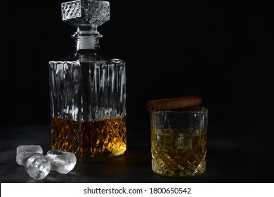 Glass Of The Whiskey With Ice Cubes And A Square Decanter, And Cigar On A Black  Background.