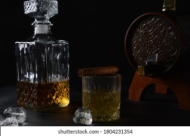 Glass Of The Whiskey With Ice Cubes And A Square Decanter, And Cigar On A Black  Background.