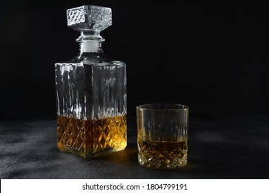 Glass Of The Whiskey With Ice Cubes And A Square Decanter On A Black  Background.