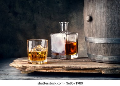 Glass Of Whiskey With Ice Decanter And Barrel On Wooden Table