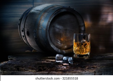 glass of whiskey with ice near the vintage barrels