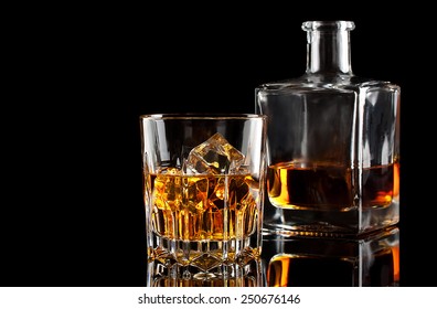 Glass Of Whiskey With Ice And A Square Decanter Isolated On A Black Background