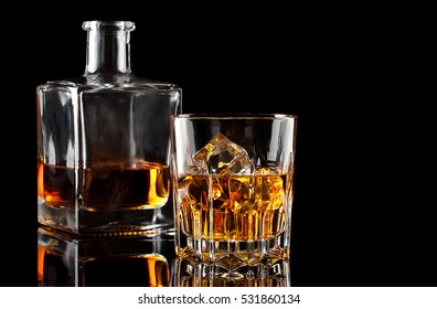 Glass Of The Whiskey With Ice And A Square Decanter Isolated On A Black Background