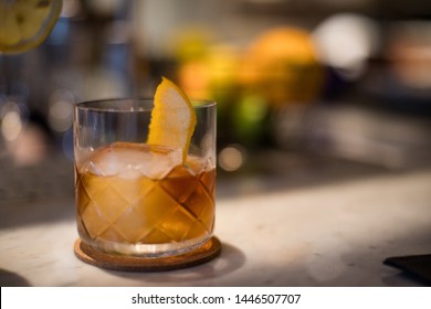 A glass of whiskey with ice stands on the bar at an expensive, upscale restaurant during happy hour.