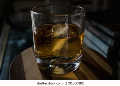 Glass Of Whiskey With Large Ice Cube On Wood Cutting Board