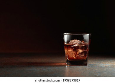Glass of whiskey with natural ice. Rough rusty background. Copy space.