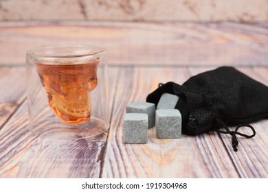A glass of whiskey next to stone cubes for cooling drinks on a wooden surface