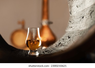 A glass of whiskey in old oak barrel. Copper alambic on background. Traditional alcohol distillery concept
