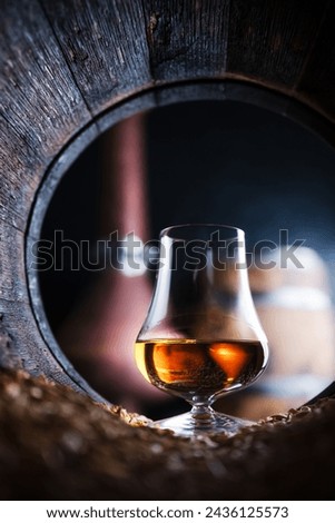 A glass of whiskey in old oak barrel. Copper alambic (distiller) on background. Traditional alcohol distillery concept