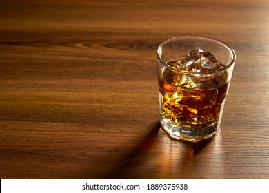 A Glass Of Whiskey On Ice On Wood Table