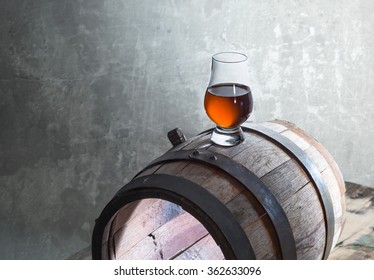 Glass Of A Whiskey On A Old Barrel On A Wall Background