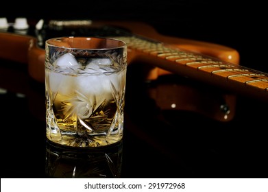 A glass of whiskey on the rocks and old guitar.