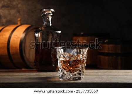 Glass with whiskey on table against wooden barrels