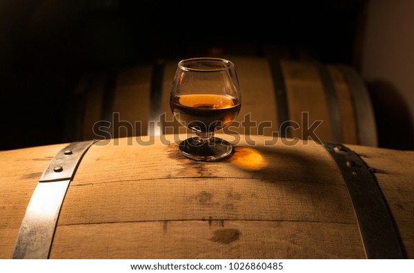 A glass of whiskey sits atop of a whiskey barrel
that is aging product. The look of the photo has a vintage feel
with a modern spirit.