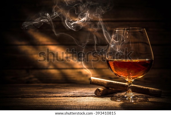 Glass of whiskey with smoking cigar and ice cubes\
on wooden table