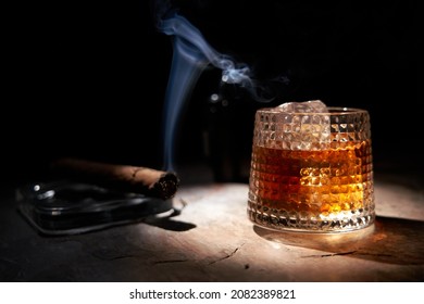 Glass of whiskey and smoking cigar on table. Copy space, black background. Whiskey, brandy, cognac, alcoholic drink .