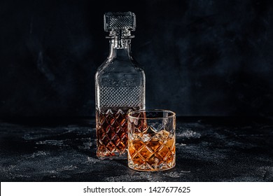 Glass Of The Whiskey With A Square Decanter On A Black Stone Background.