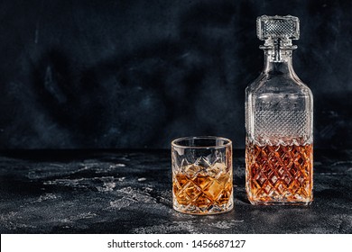 Glass Of The Whiskey With A Square Decanter On A Black Stone Background.