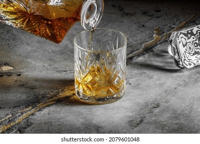 Glass of the whiskey with a square decanter on a grey clay textured  background. Pouring whiskey from decanter 