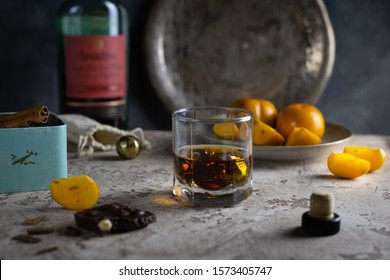
a glass of whiskey with steel balls for cooling, a plate with persimmon chocolate and a bottle