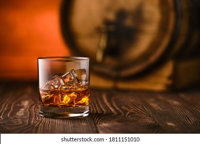 Glass of whisky with ice with barrel on background (soft focus photo with shallow deph of field)