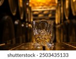 Glass of whisky with ice on old wooden barrel. Glass of whiskey with ice on table against wooden barrels background.