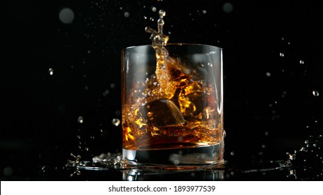 Glass Of Whisky With Splashing Liquid And Ice Rocks Inside.. Studio Shot, Isolated On Black Background