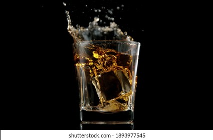 Glass Of Whisky With Splashing Liquid And Ice Rocks Inside.. Studio Shot, Isolated On Black Background