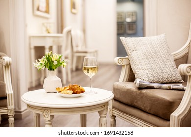 A Glass Of White Wine, Crispy Croissants And A Vase Of White Flowers Sit On The Table In The Cozy Living Room