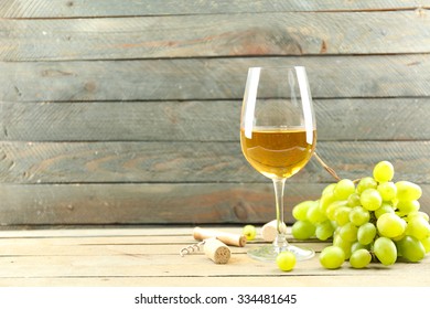 A glass of white wine and green grapes on wooden background
