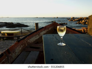 glass of white wine on the old boat table in a cafe on the beach at sunset, selective focus