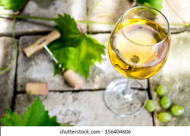 Glass of white wine on top of the background of stone, corkscrew and cork, vine leaves and grapes.