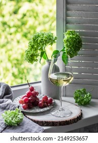 Glass Of White Wine And Red Grapes On The Window In The Cozy Room - A Delicious Aperitif, Snack      