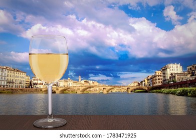 Glass of white wine with view of bridge in Florence during sunset - Ponte alla Carraia,  five-arched bridge over Arno River in the Tuscany region of Italy. Beautiful blue with pink sky with clouds. 