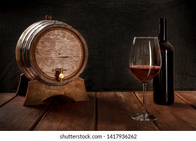 A Glass Of Wine With A Bottle And A Wine Barrel, Side View On A Dark Rustic Background, Low Key Photo With A Place For Text