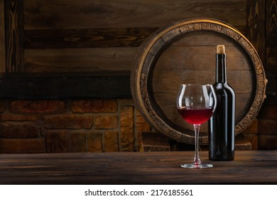 A glass of wine, a bottle of red wine chardonnay in front of the rustic barrels for a beverage in a dark wine cellar. Wooden empty surfaces for copy space, mock-up, and template for the design of wine