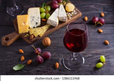 Glass Of Wine With Cheese, Grapes, And Nuts On Black Wooden Table. Wine And Food. View From Above, Top Studio Shot