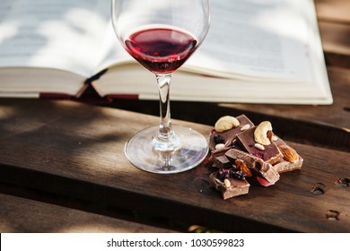 Glass with wine and pieces of chocolate near open book